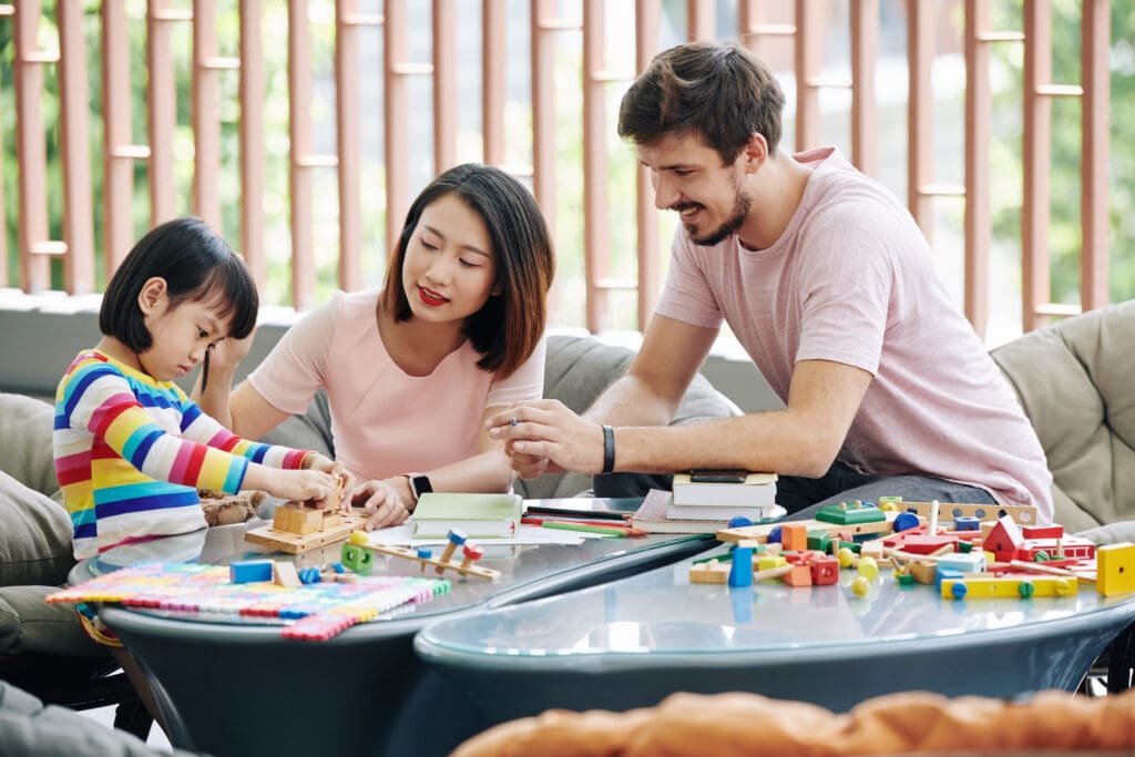 Happy young parents helping daughter to find solution for toy puzzle